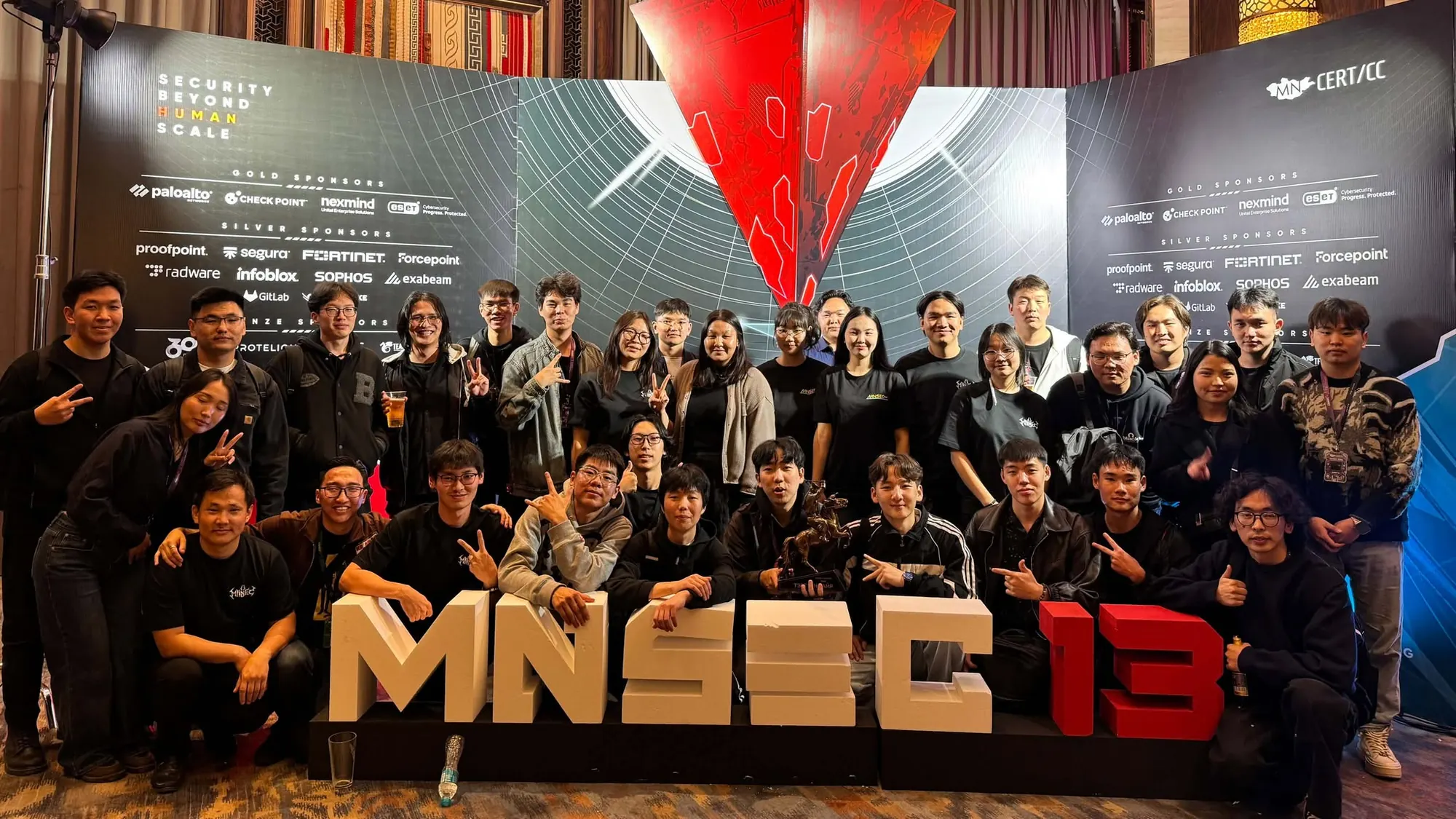 A group poses behind large MNSEC 13 letters, with a trophy held in the front row.